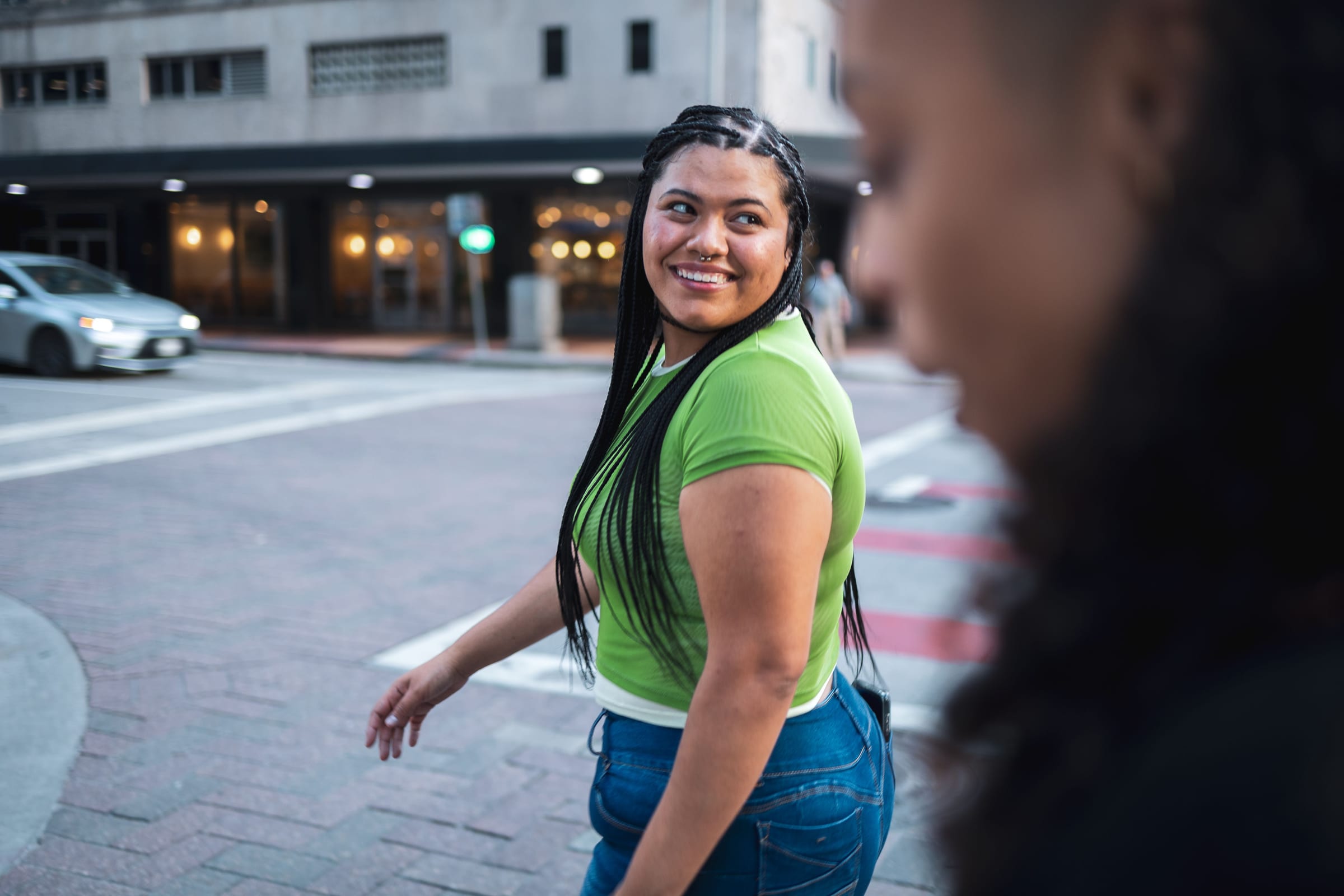 a young woman glancing back with a smile as she crosses a city street